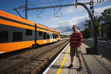 Naklejka premium A man with a beard and sunglasses waits for a train on the platform on a summer day in Tallinn.