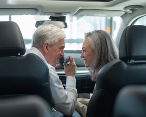 Mature Caucasian couple sitting in a new car and rejoicing at the purchase. 