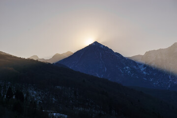 Winter sun behind a mountain peak of a winter alpine landscape at Barcis, Friuli-Venezia Giulia,...