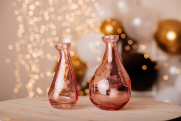 A pair of elegant pink glass vases on a wooden table with festive blurred golden and white lights in the background, perfect for home decor or celebrations.