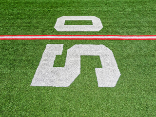 Football Field Turf. Bright green turf football field with red and white yard line markings. Focus...