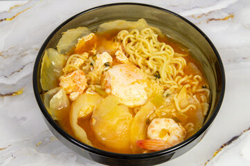 A bowl of soup with noodles and shrimp. The soup is orange and has a lot of noodles