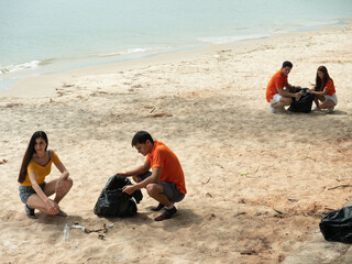 Fototapeta na wymiar Two young couple of volunteers cleans plastic and garbage in a black trash bag on a tropical beach..
