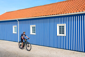 nice woman cycling with her electric mountain bike in front of the colorful wooden houses of Costa...