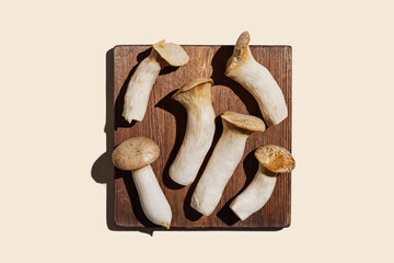 Pleurotus eryngii white mushrooms with shadows on wood, edible fungus as minimal flat lay on beige background, top view pastel color still life from whole mushroom at sun light, alternative proteins