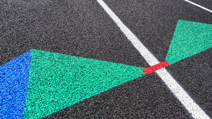 Fototapeta na wymiar Angled overhead view of a rubber black running track surface with white lane lines. Green and blue arrows point forward. Red dashed line between the arrow shapes. Texturized rubber black surface.