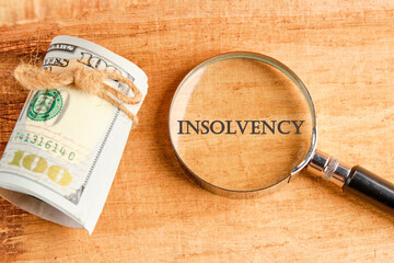 Debt relief concept. A word INSOLVENCY through a magnifying glass, they are visible on a beautiful background next to a roll of paper banknotes