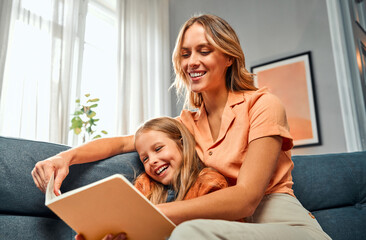 Story time with mom. Attractive mother sitting with daughter in cozy room and reading book