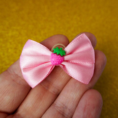 On a yellow background, in your hand lies a small pink bow with a strawberry in the middle. view...