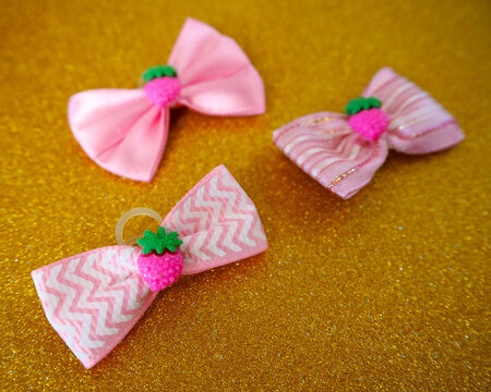 Three different pink bows with a pink strawberry in the middle lie on a gold background. Side view. Accessories for small dogs. Top notes