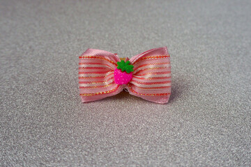 Fototapeta na wymiar on a gray background, a pink bow with white stripes with a bright pink strawberry in the middle. side view . accessories for pets with long hair. top notes for dogs