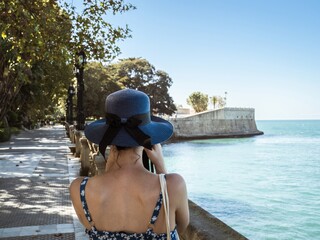 A young girl in a blue dress and hat taking a photo of the city walls with the bastion Baluarte de...