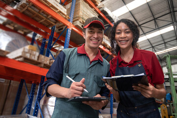 Two warehouse workers in their work clothes smile happily at the camera, work together in a large...