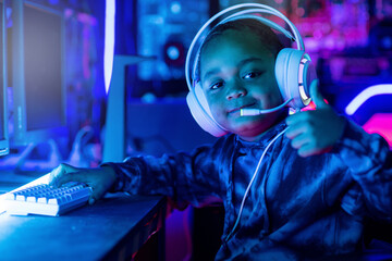 African boy wearing headphones shows thumbs up at camera after finishing playing video game,...