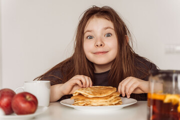 Little cheerful teenage girl preparing to eat a stack of pancakes for breakfast. High quality photo
