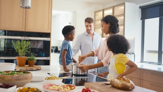 Children helping parents in kitchen as family prepare food for meal together - shot in slow motion