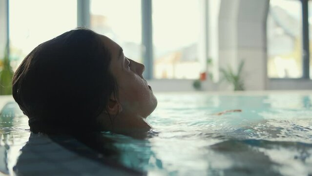 A serene image capturing a female figure swimming leisurely in an enclosed pool area with natural light casting over the water