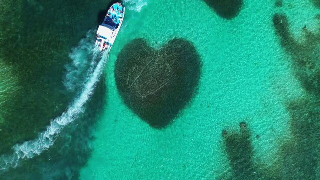 Aerial top view at Heart-shaped barrier reef coral. Turquoise ocean water. Tropical paradise. Catamaran boat with tourists. Caribbean Sea. Atlantic ocean. Zoom out.