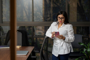Mexican business woman checking her cell phone in the office