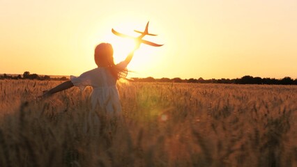 Adorable female kid silhouette running with aircraft toy at cinematic sunset sunrise wheat field...