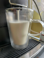 Coffee with milk poured from a coffee machine into a transparent, double-walled thermal mug