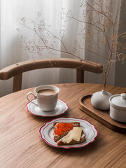 Delicious breakfast, snack - a cup of coffee and red caviar and cheese sandwiches on a round wooden table