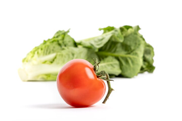 A ripe red tomato on the vine with romaine lettuce out of focus in the background isolated on white