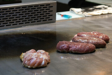 cooking, slicing, cutting and grilling raw uncooked duck breast and beef in a Japanese teppanyaki restaurant being cooked by a chef with blue gloves in a kitchen