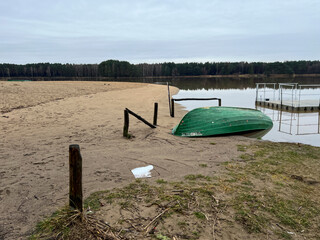A boat lying upside down on the beach of a small lake in early spring after the snow and ice have gone - 778351537
