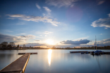 View from the shore into the distance and a sunset at the lake. The surroundings and the beautiful sky are reflected in the water. A great landscape shot
Dutenhofener See, Hesse Germany - obrazy, fototapety, plakaty
