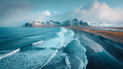 Drone view of rocky mountains covered in snow near waving seawater along black sand beach in Iceland, eystrahorn, krossanesfjall, iceland, against cloudy skies - Powered by Adobe