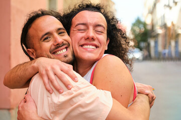 Gay man hugging his boyfriend at street. They are smiling and seem happy.