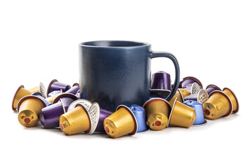 A blue coffee mug surrounded by a pile of colorful used espresso coffee maker pods isolated on white
