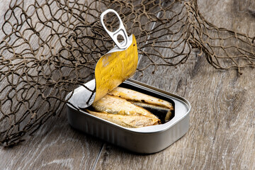 An opened can of sardines with a ring pull top on a wooden surface such as a dock wrapped in...
