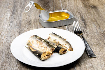 A plate of tinned sardines and an empty ring pull tin in the background on a rustic wooden surface like a fishing pier