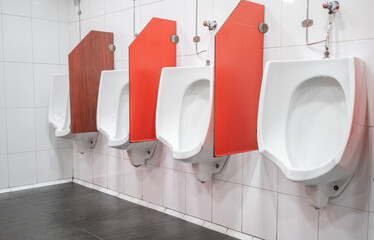 Side view of a white-walled public restroom with four symmetrical urinals in a row. They have red...