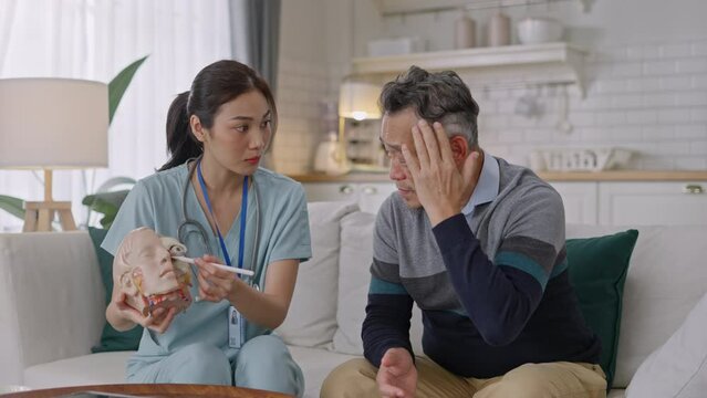 Doctor explain and discuss with senior asian patient of head and maxillary sinuses with Nasal and oral cavity anatomical model on sofa in living room during home visit.Doctor Taking Home Medical Care