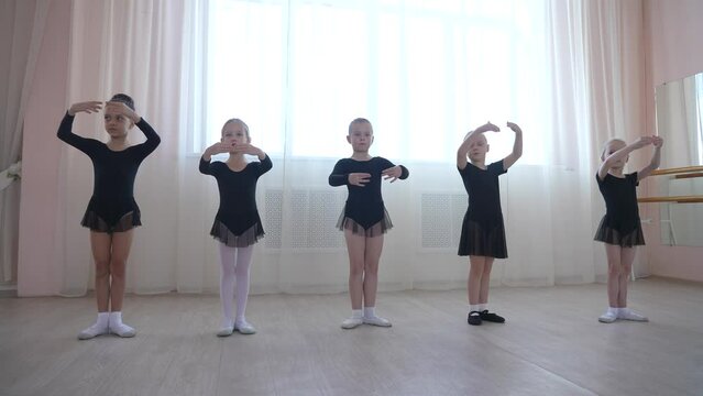 Cute little girls in black swimsuits and tutu practice ballet in class. 