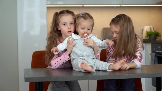 Sisters laugh and tickle funny playing with little baby at home. Girls looking after baby. Happy family concept. Active childrens games, leisure