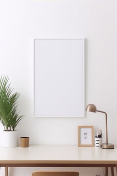 White desk with a potted plant, a lamp, a picture frame and a cup with pencils on it against a white wall in a minimalist home office.
