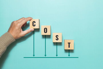 Concept of cost, lean or cost reduction. Hand placing a wooden block with the word cost and down...