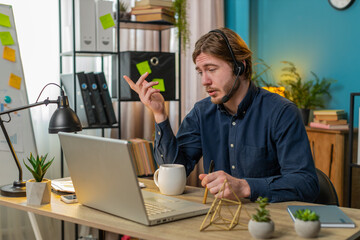 Fototapeta premium Caucasian businessman wearing headset, freelance worker, call center or support service operator helpline, talking with client or colleague communication support. Happy man sits at home office desk.