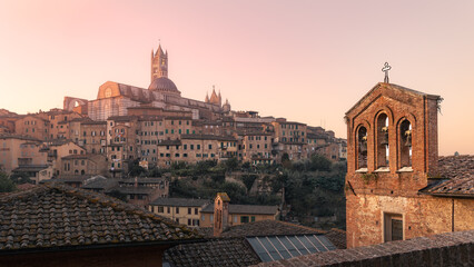 Obraz premium Ancient town with cathedral, bell tower surrounded by residential buildings at sunrise, Siena, Italy