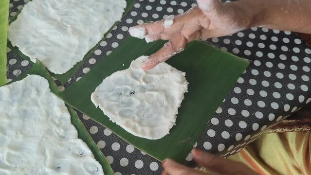 a person spreading food batter in a banana leaf with hand, a traditional way of cooking organic sweet indian dosa dish