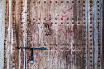 A weathered traditional locked arabian door with rusted doornails and door knocker.