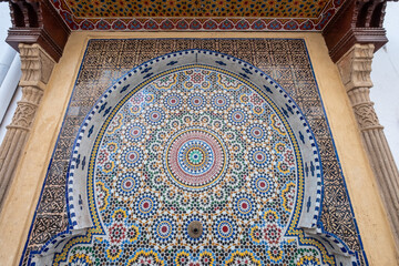 Detailed islamic geometrical mosaic patterns cover a wall with the brass spout of a public water fountain