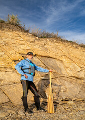 senior male paddler wearing life jacket with a wooden canoe paddle on a rocky lake shore