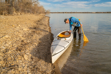 senior male paddler with expedition decked canoe on a lake shore in early spring, Boedecker...