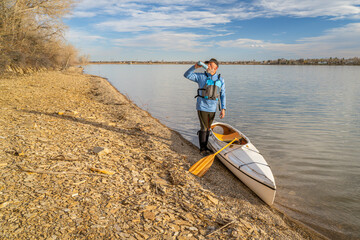 senior male paddler with expedition decked canoe on a lake shore in early spring, Boedecker Reservoir in northern Colorado