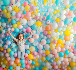 Fototapeta na wymiar A happy little girl in an overhead shot, with a big smile and open arms among a bunch of colorful balloons and confetti with space for text. Illustration for birthdays, mother's day, celebrations...